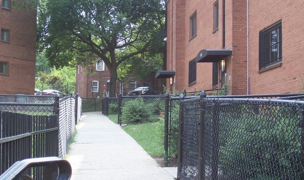 A black fence runs along a sidewalk in front of a brick building.